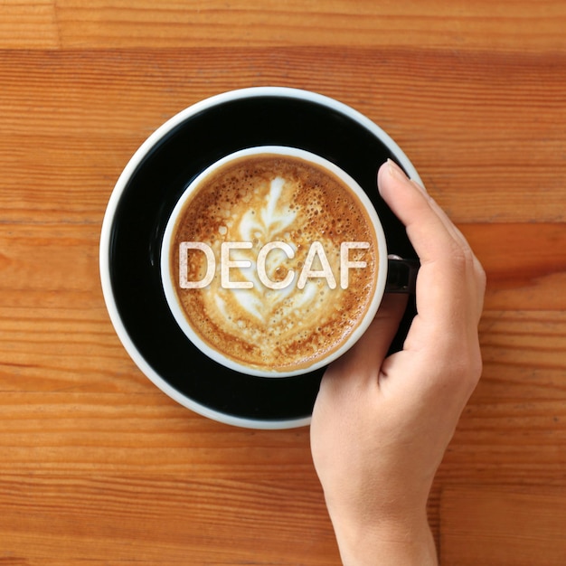 Woman with cup of aromatic decaf coffee at wooden table top view