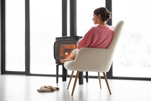 Woman with cup on chair by the fireplace at house on nature