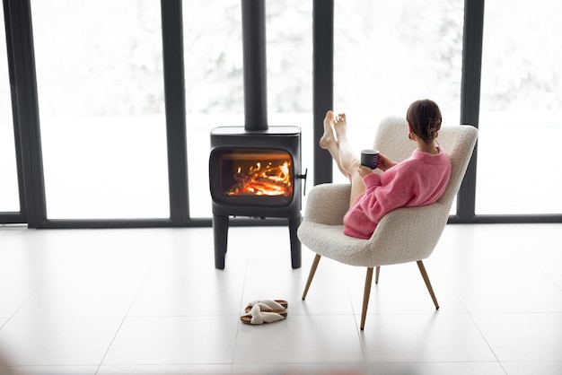 Woman with cup on chair by the fireplace at house on nature