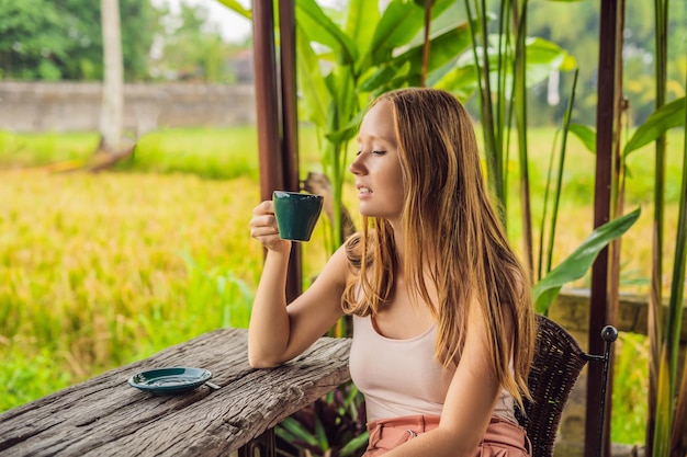 Woman with a cup of coffee on the cafe veranda near the rice terraces on Bali, Indonesia.