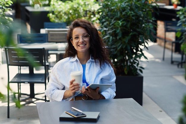 Woman with cup of coffee working at outdoor cafe in morning