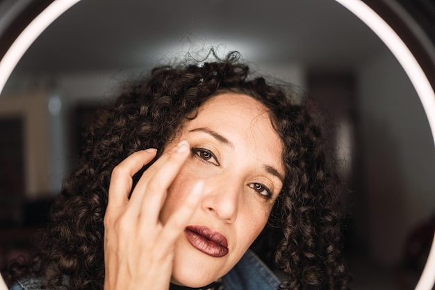 A woman with curly hair applies a liquid foundation on her face.