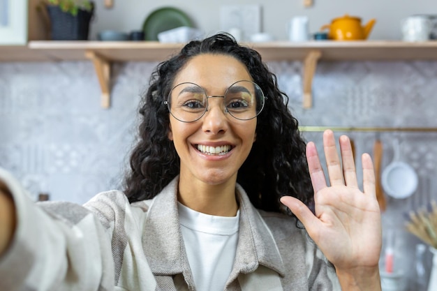 Woman with curly hair and glasses looking into smartphone camera taking selfie and talking on video