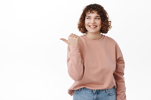 woman with curly hair, looking and pointing left with happy smile with joyful expressionon white.