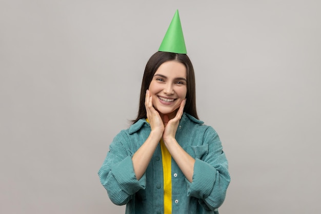 Woman with dark hair in birthday party cone and smiling to camera enjoying birthday celebration