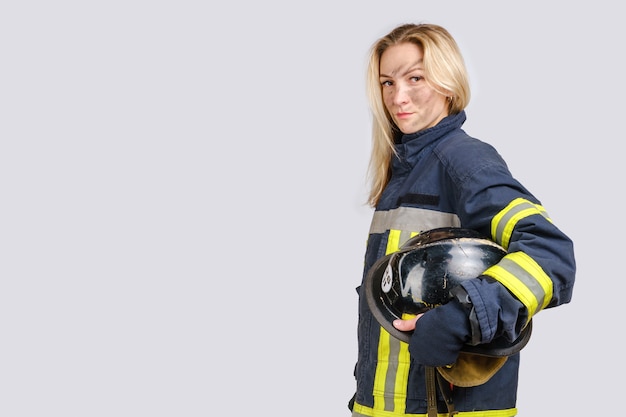 woman with dirty face in uniform of firefighter holds hardhat in hand