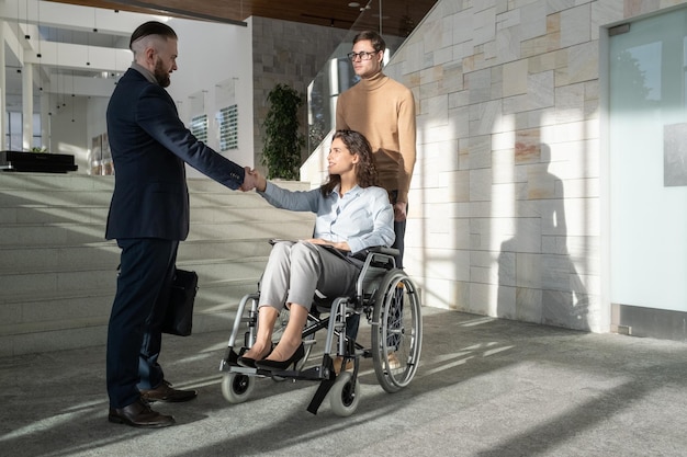 Woman with disability sitting in wheelchair while handshaking with partner