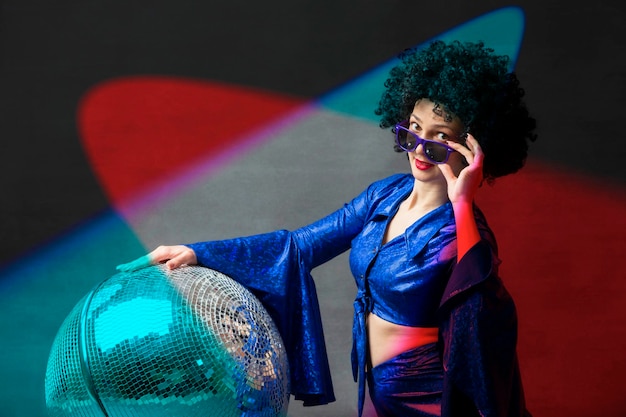 A woman with a disco ball in an afro wig in multicolored rays of light