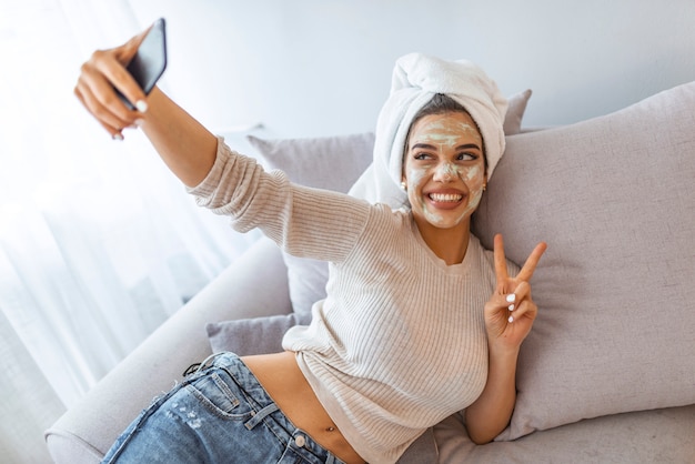 Woman with facial clay mask making selfie on her smartphone