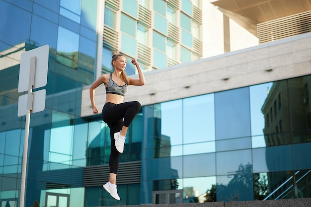 Woman with fit body jumping and running against urban city background