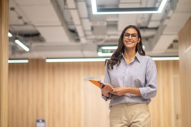 Woman with folder smiling at camera indoors