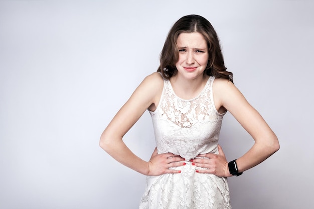 Woman with freckles and white dress and smart watch with stomach pain on silver gray background