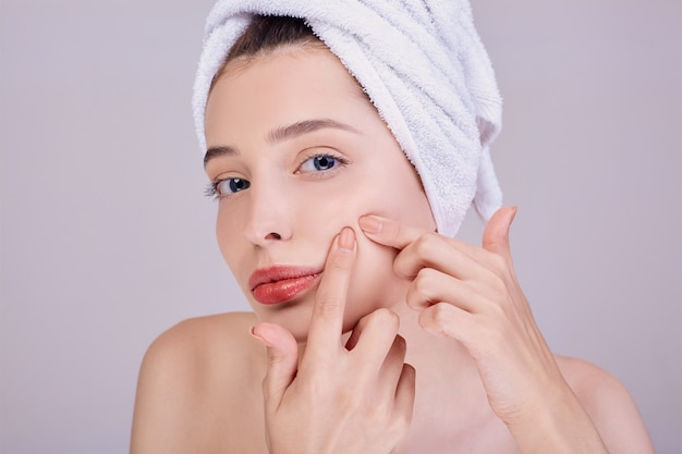 A woman with full lips crushes a pimple on her cheek.