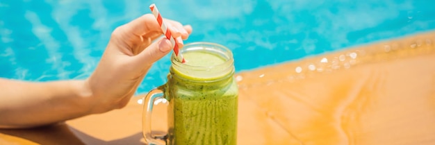 Woman with a green smoothies of spinach and banana on the background of the pool healthy food