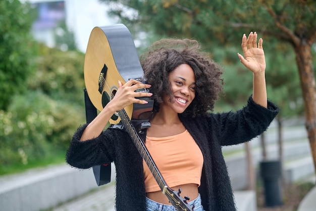 Woman with guitar on shoulder raising hand in greeting