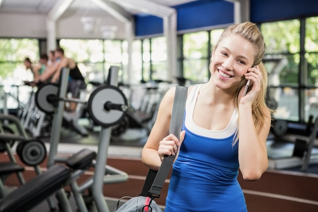 Woman with gym bag talking on the phone in weights room