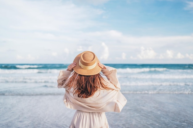 Woman with hat relaxing with her arms raised to her head enjoying looking view of beach summer day