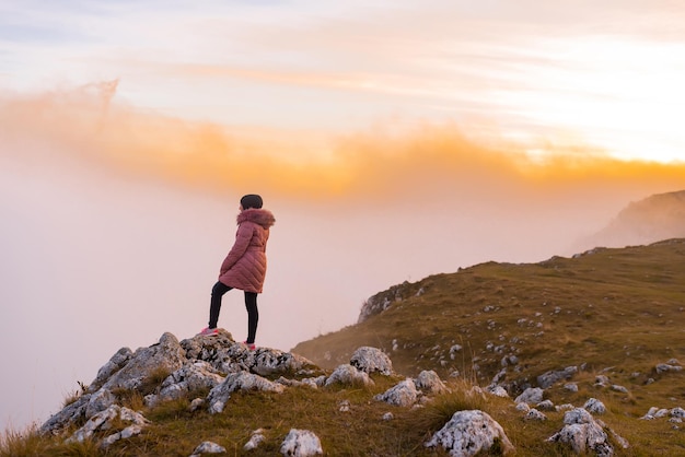 Woman with a head scarf standing alone on the top mountain cliff peak at sunset