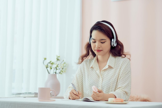 Woman with headphones and a diary eating macarons in living room