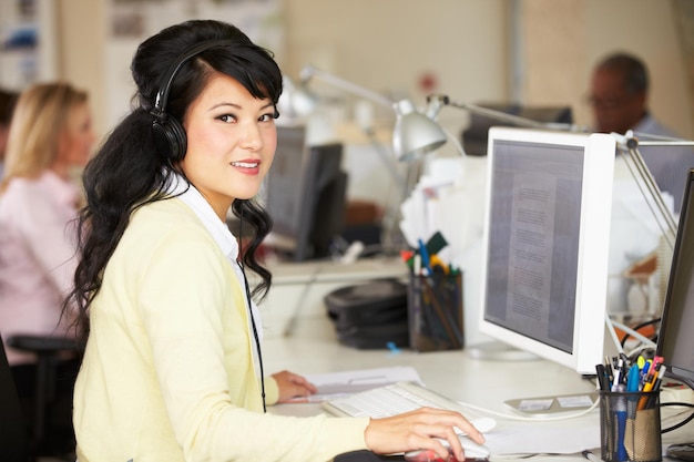 Woman With Headset Working At Desk In Busy Creative Office