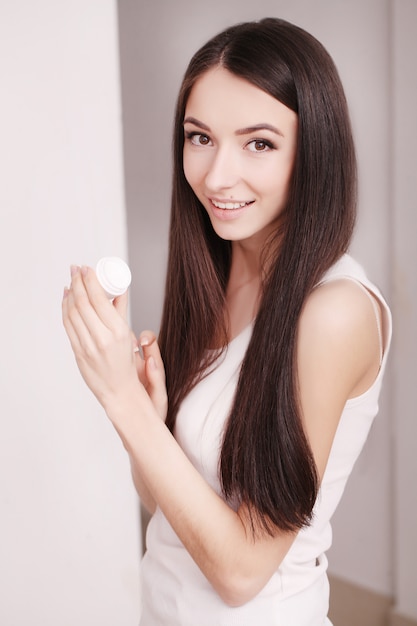 Woman with healthy face applying cosmetic cream under the eyes