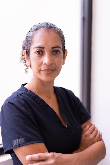 A woman with her arms crossed stands in front of a white wall.