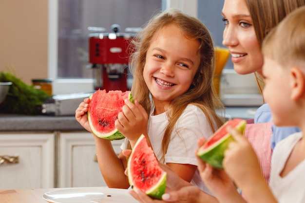 Woman with her daughter and son eating watermelon in kitchen