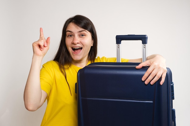 A woman with her mouth open shows a thumbs up hugging a travel suitcase