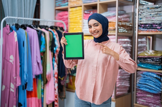 Woman with hijab showing her blank screen to camera while working at her fashion warehouse online se