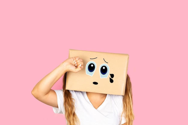 Woman with his head in a box and crying gesture standing on a pink background with copy space