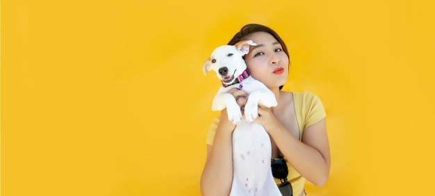 Woman with jack russel puppy embraces with love dog takes care of pet wears casual clothing on yellow isolated background copy space for your promo