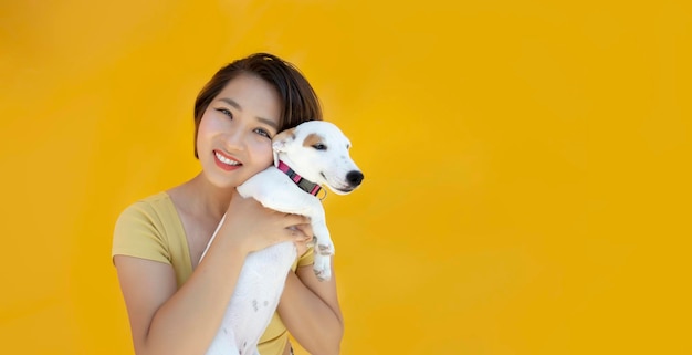 Woman with jack russel puppy embraces with love dog takes care of pet wears casual clothing on yellow isolated background copy space for your promo