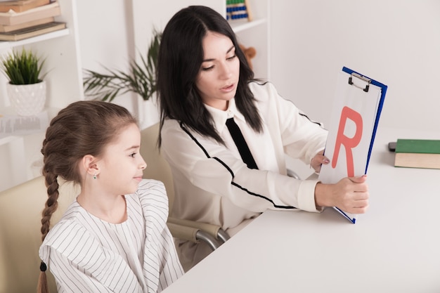 Woman with kid girl training speech together sitting in the white room.