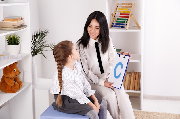 Woman with kid girl training speech together sitting in the white room.