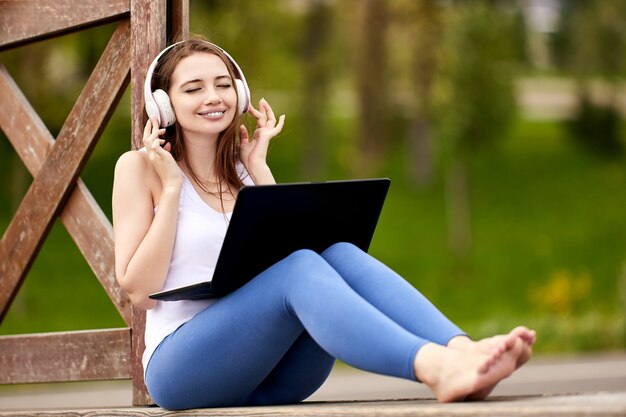 Woman with laptop in cordless headphones during teleworking outdoors