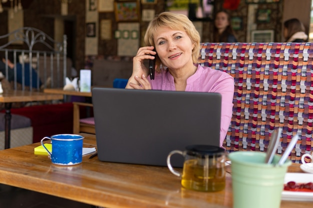 A woman with a laptop is working in an office. A middle-aged woman is a businesswoman in a cafe. She smiles. She's on the phone.She looks at the computer.