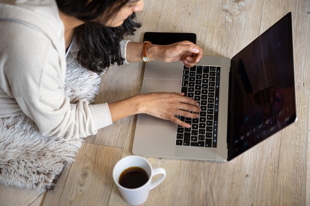 Woman with laptop online at home drinking coffee, with cell phone