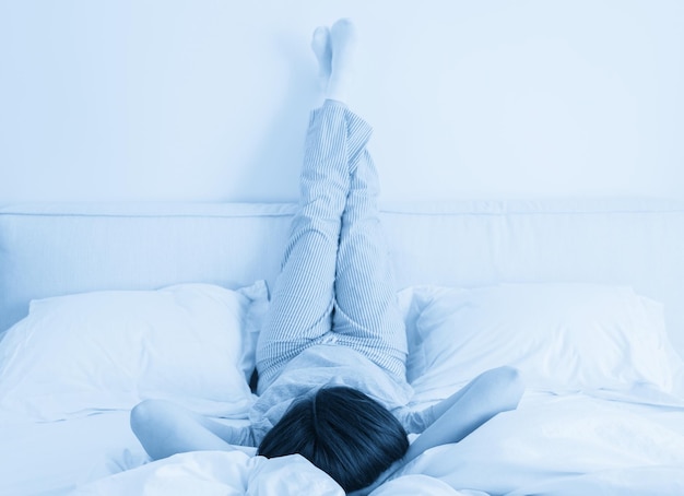 Woman with legs raised up high and arms under her head lying on bed in bedroom