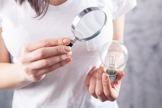 Woman with a magnifying glass looks at a light bulb. concept study idea