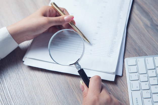 Woman with a magnifying glass looks at paper on the desktop