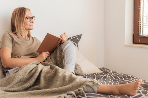 Woman with medical mask at home reading book in quarantine