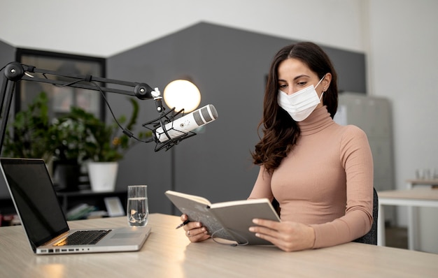 Woman with medical mask in a radio studio with microphone and laptop