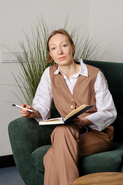 Woman with notebook and pen sits in armchair and listens attentively to interlocutor