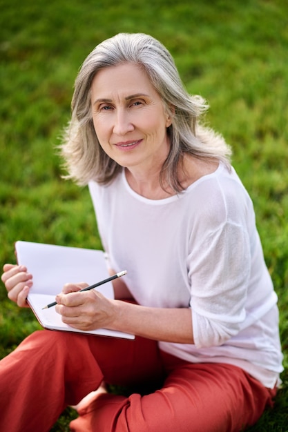 Woman with notebook and pencil sitting on grass