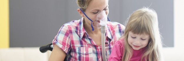 Woman with an oxygen mask and in wheelchair is reading book with little girl