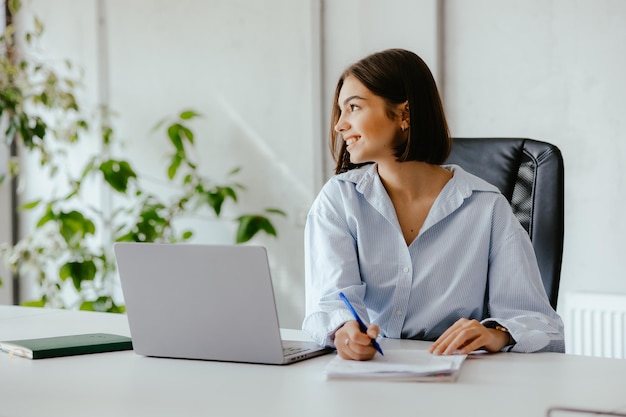 Woman with papers in an office working at her desk with a laptop in front of her