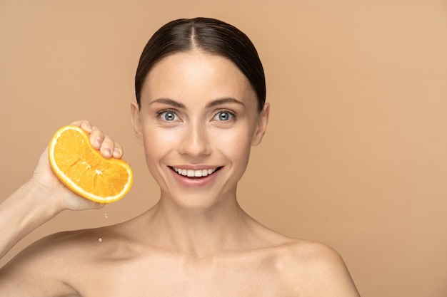 Woman with perfect face skin, combed hair, squeezing orange. Smiling female with natural makeup and citrus fruit