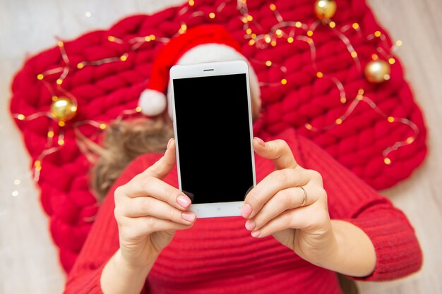 Woman with phone copyspase in hand santa hat lie on a soft merino wool blanket.