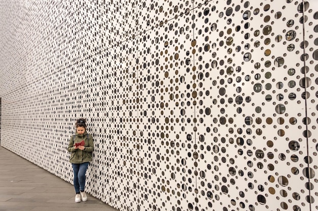 A woman with a phone near the wall of the building.