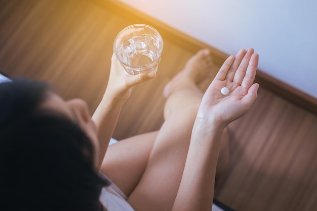 Woman with pills or capsules on hand and a glass of water